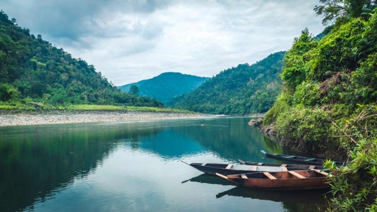 Two boats are docked on the river in Dawki, with a scenic mountain backdrop.