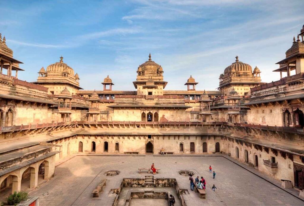 Ornate courtyard of an Indian palace in Orchha fort complex, surrounded by lush gardens and historical architecture.
