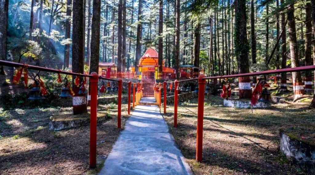 A serene forest path leading to the red Tarkeshwar Mahadev Temple shrine in Lansdowne, surrounded by lush greenery.