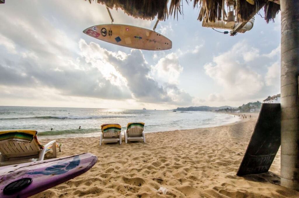 Surfers riding waves at Playa Zipolite beach in Puerto Vallarta, Mexico, under a clear blue sky.