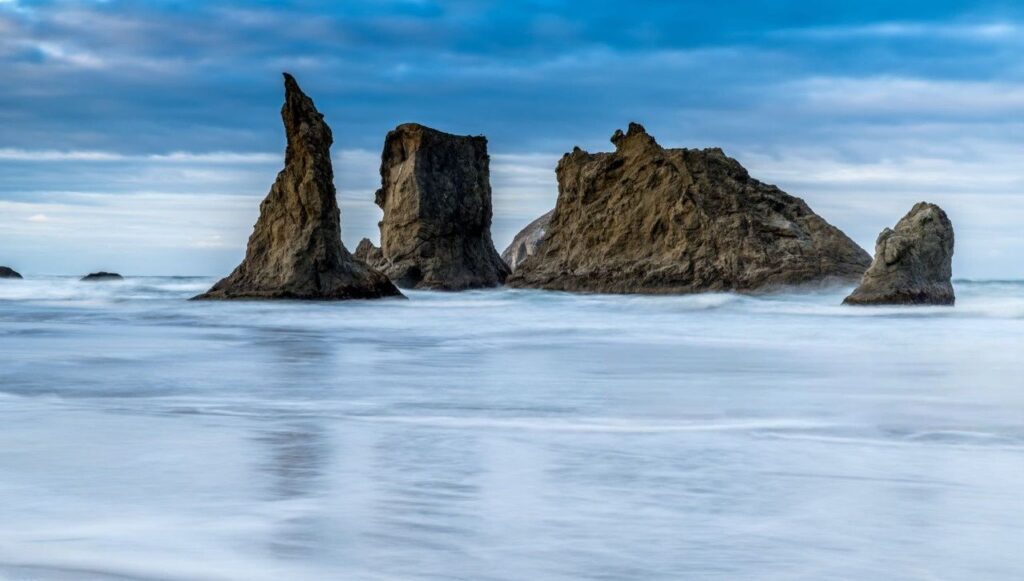 Three rock formations on Bandon Beach silhouetted against a vibrant sunset sky.
