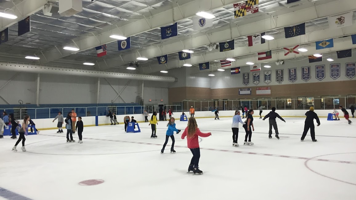 Extreme ice centre,People of all ages enjoy public ice skating in an indoor rink with flags and banners above them.