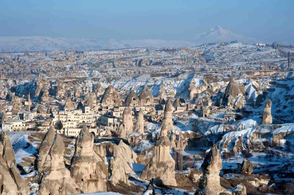 A scenic view of Zemi Valley in Cappadocia, featuring snow-draped mountains and charming buildings.