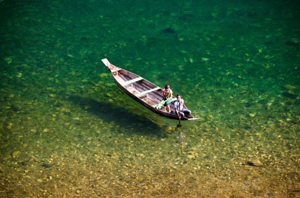 Two visitors riding a boat in crystal clear water of the Umngot River in Dawki and boat is looking like it floating in air