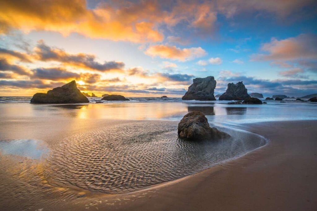 Sunset over Bandon Beach, featuring rocky formations and gentle waves lapping at the shore.